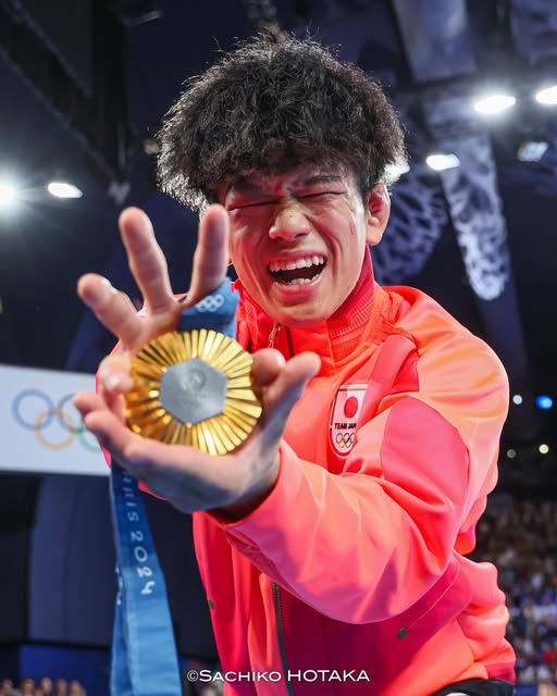 Kotaro Kiyooka smiling and holding his Paris gold medal toward the camera